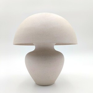 May include: A white ceramic table lamp shaped like a mushroom. The lamp has a rounded top and a bulbous base.
