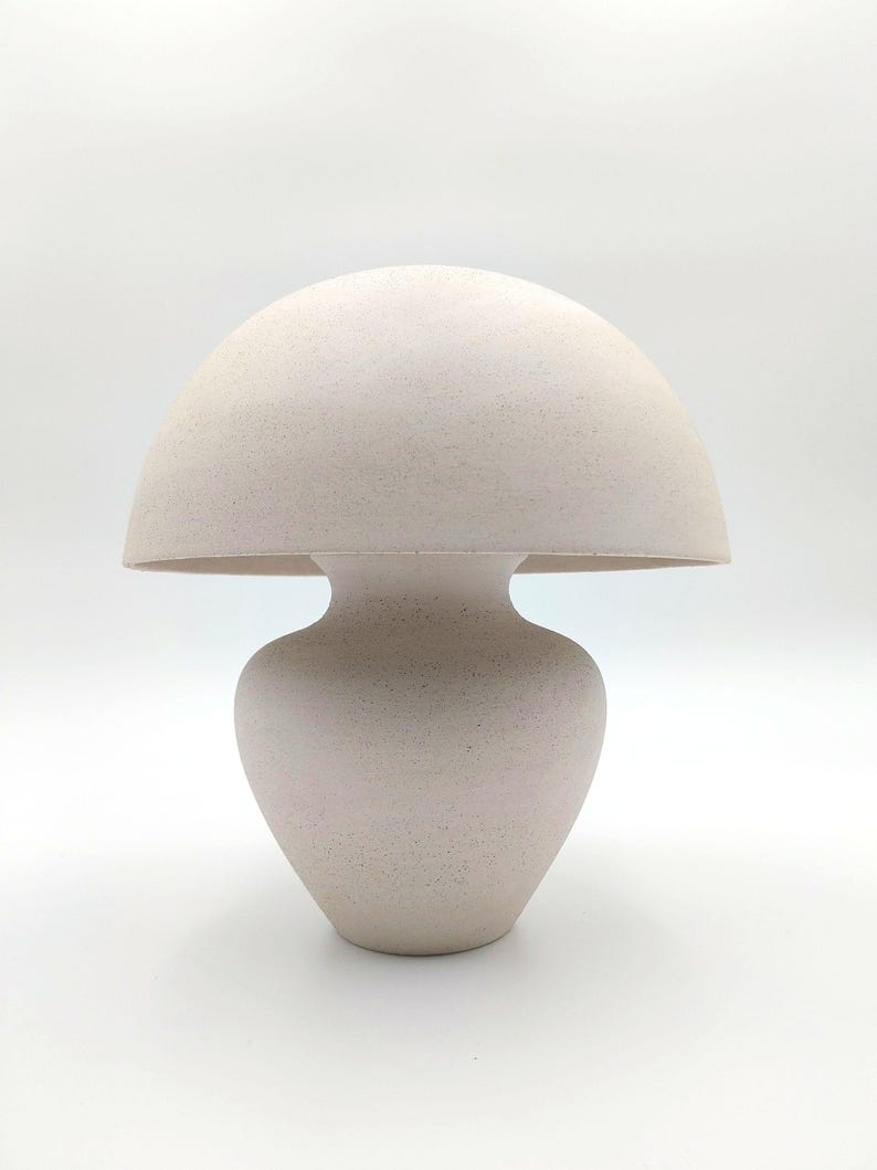May include: A white ceramic table lamp shaped like a mushroom. The lamp has a rounded top and a bulbous base.