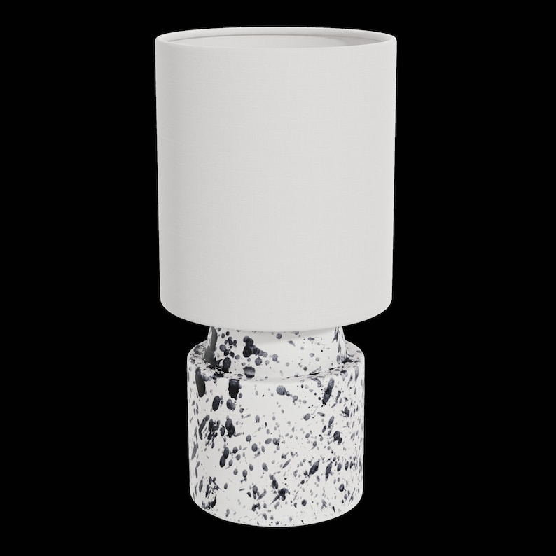 May include: A white ceramic table lamp with a white fabric shade. The base of the lamp has a black and white splatter paint design.
