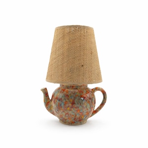 Könnte beinhalten: Eine dekorative Tischlampe mit einem bunten, gesprenkelten Keramik-Teekannenfuß. Die Lampe hat einen Ausguss und einen Henkel. Der Lampenschirm ist beige und gewebt. Ein dekoratives Element für die Inneneinrichtung.