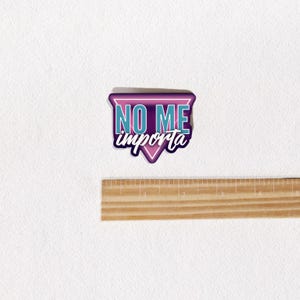May include: A pink and blue triangle sticker with the text "NO ME importa" in white.