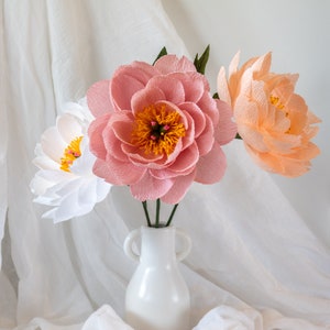 Puede incluir: Tres flores de papel en un jarr&oacute;n blanco. Las flores son rosas, melocot&oacute;n y blancas. Las flores est&aacute;n dispuestas en un ramo.