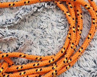 May include: Orange and black rope with a diamond pattern. The rope is coiled on a white fuzzy surface.