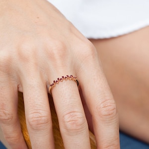 Könnte beinhalten: Ein zarter Goldring mit einer Reihe kleiner roter Edelsteine. Der Ring wird am Ringfinger einer Hand getragen.
