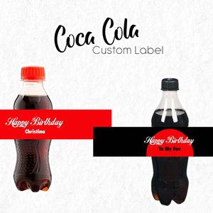 Könnte beinhalten: Zwei Coca-Cola-Flaschen mit individuellen Etiketten. Die erste Flasche hat ein rotes Etikett mit dem Text "Happy Birthday Christina". Die zweite Flasche hat ein schwarzes Etikett mit einem roten Kreis, auf dem "Happy Birthday To My Fav" steht.