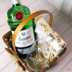May include: A gift basket with a bottle of gin, a glass, and a wrapped gift box. The bottle is labeled "Suzanne Happy 50th Birthday".