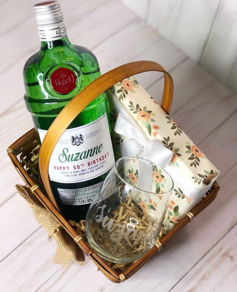 May include: A gift basket with a bottle of gin, a glass, and a wrapped gift box. The bottle is labeled "Suzanne Happy 50th Birthday".
