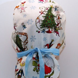 May include: A blue and white scrub hat with a Christmas tree and characters from the book "How the Grinch Stole Christmas!" printed on it. The hat has a blue tie.
