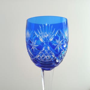 Puede incluir: Primer plano de una copa de vino de cristal azul cobalto. La copa presenta intrincados patrones de corte en forma de estrella y diamante. El tallo es transparente y la copa es de un azul vibrante y transparente. La copa está diseñada para servir vino.