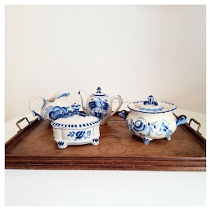 May include: A set of white ceramic tea service items with blue floral patterns, including a teapot, creamer, sugar bowl, and a lidded dish, presented on a wooden tray with brass handles. The design is classic and vintage.