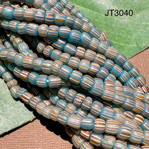 Puede incluir: Primer plano de un montón de cuentas de vidrio azul turquesa con rayas multicolores. Las cuentas son opacas y tienen un acabado brillante. Las cuentas están dispuestas en un patrón aleatorio. JT3040