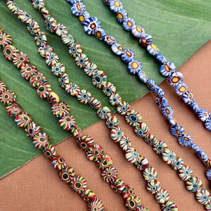 May include: Close-up of several strands of colourful glass beads. The beads are flower-shaped with red, green, yellow, and blue patterns. The beads are strung together, creating a vibrant and decorative accessory.