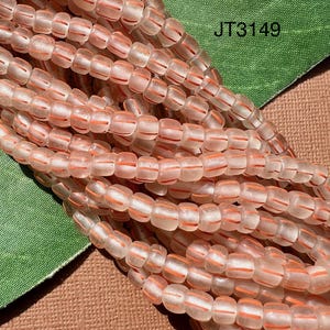 May include: A strand of translucent glass beads with thin, opaque orange stripes. The beads are approximately 6mm in diameter and have a slightly rounded, rectangular shape.