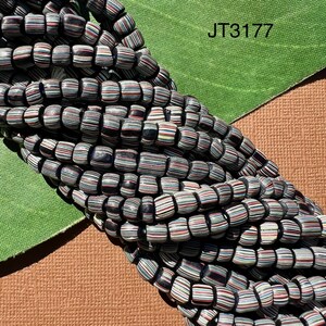 May include: A strand of black, white and red striped glass beads. The beads are cylindrical and have a slightly rounded shape. The beads are arranged in a pile, with some of the beads overlapping.