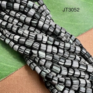 May include: Close-up of a strand of beads. The beads are cylindrical, with a pattern of black, white, and gray stripes. The beads are strung together on a black cord. The text "JT3052" is visible in the upper right corner.