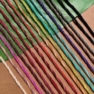 May include: A collection of colorful twisted cords in various shades, including red, green, yellow, and purple. The cords are arranged diagonally against a brown and green background, creating a visually appealing pattern. The cords appear to be made of a woven material.