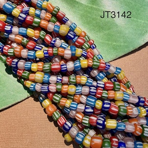 May include: A collection of multi-coloured glass beads arranged in several strands. Each bead features a striped pattern with white lines against vibrant colours including red, blue, green, yellow, and orange. The text JT3142 is visible.