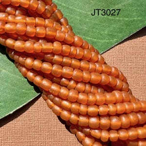 Peut inclure: Un brin de perles de verre orange. Les perles sont petites et ont une finition mate. Les perles sont disposées en un tas lâche. L'image comprend le texte "JT3027".