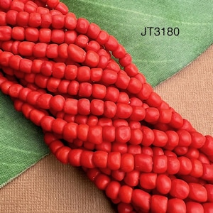 May include: Close-up of strands of bright red beads. The beads are small, rectangular, and strung together. The image includes the text "JT3180" in the upper right corner. The beads are displayed against a green and tan background.