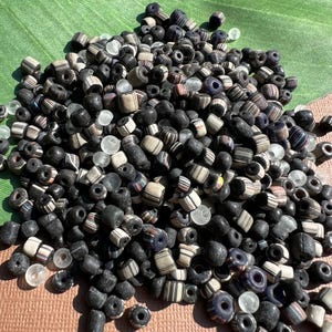 May include: A large pile of black and white striped glass beads with a few clear glass beads mixed in.