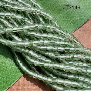 May include: A close-up of a strand of green and white glass beads. The beads are small and round, and they are arranged in a random pattern. The beads are translucent, and they have a slight shimmer to them.