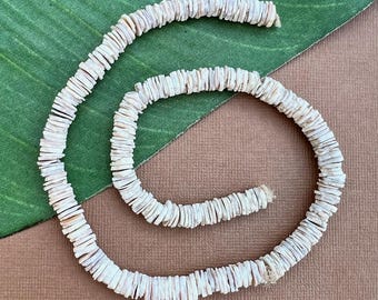 May include: A strand of white shell beads, made from flat, oval-shaped pieces of shell. The beads are strung together to form a long necklace.