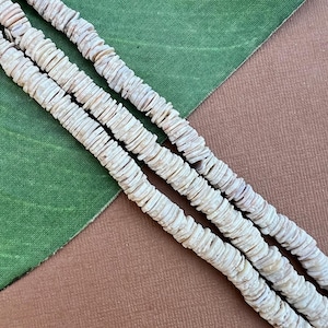 May include: A strand of white shell beads, made from natural materials, with a smooth, polished finish. The beads are arranged in a symmetrical pattern, creating a visually appealing and elegant look.