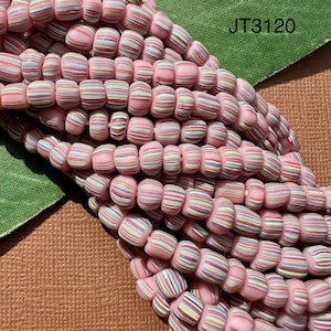 May include: A close-up of a strand of pink and white striped glass beads. The beads are small and round, and they are arranged in a random pattern. The beads are strung on a clear thread.