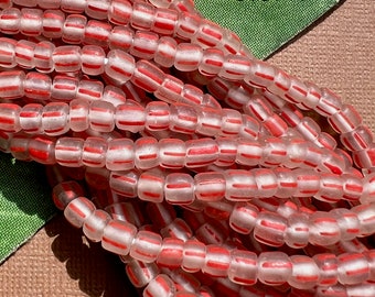 May include: A strand of translucent white glass beads with red stripes. The beads are small and cylindrical in shape.