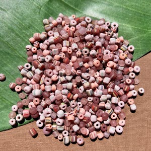 May include: A large pile of pink, white and multi-coloured glass beads. The beads are small and round, and they are perfect for jewellery making.