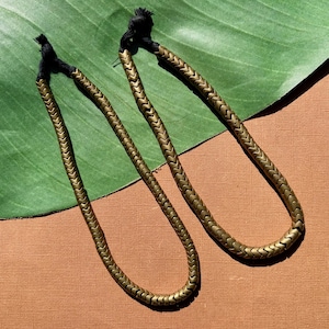 May include: Two matching necklaces featuring a continuous strand of metallic bronze-toned chevron-shaped beads. Each necklace is finished with a black knotted cord at the top, creating a flexible loop design that hangs in a rounded shape.