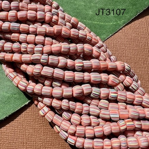 May include: A close-up of a strand of pink and white striped glass beads. The beads are small and round, and they are arranged in a random pattern. The beads are perfect for making jewelry or other crafts.
