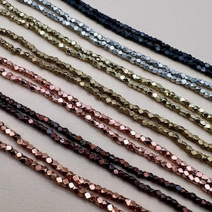 May include: Close-up of multiple strands of faceted beads in various metallic colors, including black, silver, gold, bronze, and copper. The beads are strung together, creating a textured and shimmering effect, ideal for jewelry making.