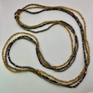 May include: A multi-strand beaded necklace with a mix of gold, brown, and colourful beads. The necklace features a variety of small, round beads in shades of gold, brown, red, blue, and green. The strands are connected with a gold-coloured ring.