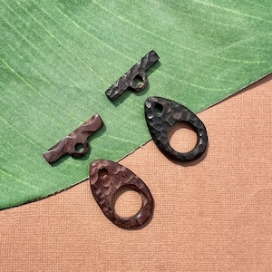 May include: Three wooden toggles with a textured finish. Two are oval shaped with a hole in the center. One is a rectangular shape with a hole in the center.