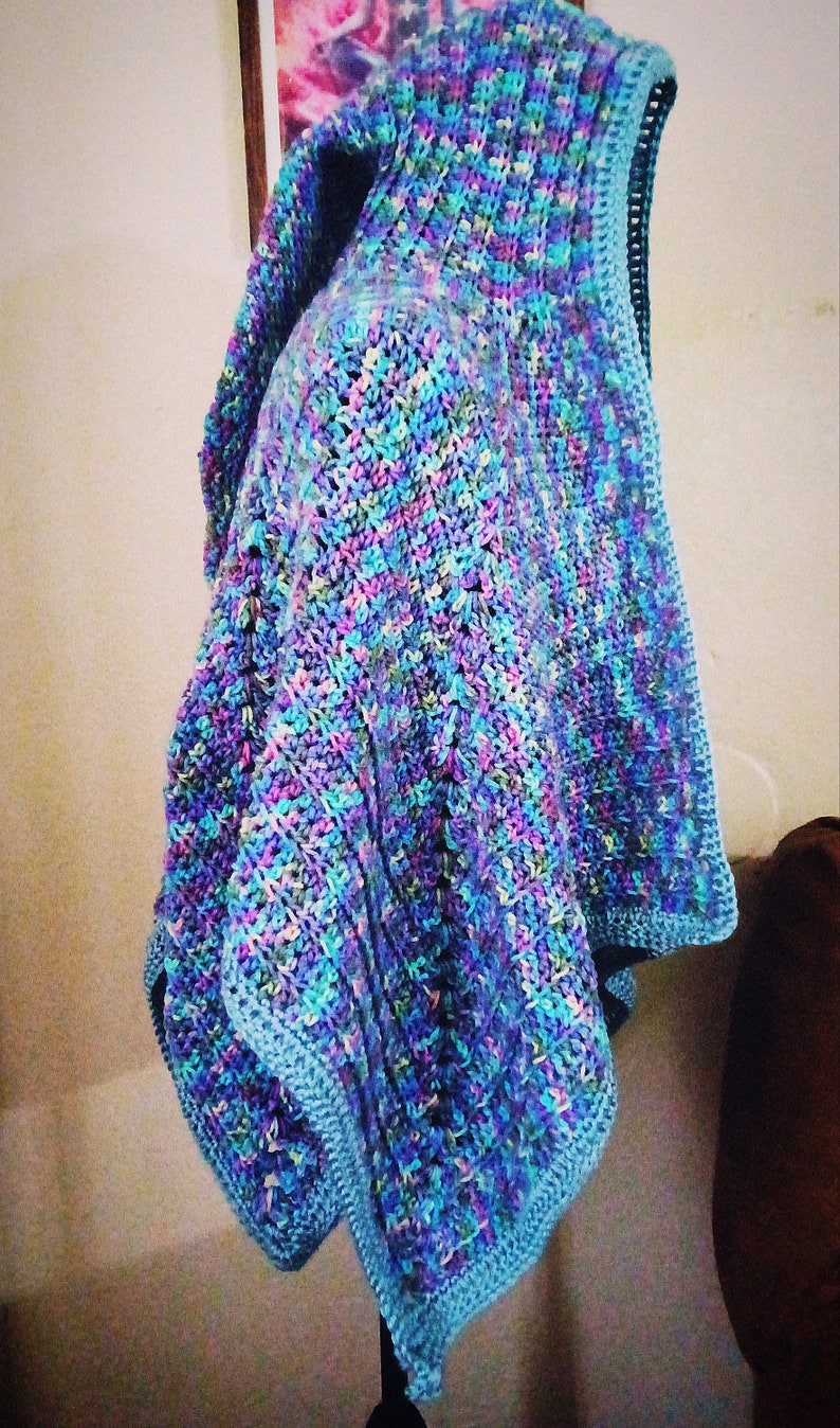 K&ouml;nnte beinhalten: Ein geh&auml;keltes Tuch in Blaut&ouml;nen, Lila und Gr&uuml;n. Das Tuch hat eine Kapuze und ein strukturiertes Stichmuster.