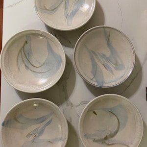May include: Five white ceramic bowls with blue and gold marbling. The bowls are all the same size and shape, and they are arranged in a circle.