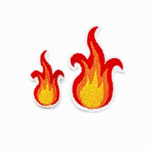 Könnte beinhalten: Zwei gestickte Flammenaufnäher in unterschiedlichen Größen mit einem lebendigen Farbverlauf von Gelb an der Basis bis hin zu Orange und Rot an den Spitzen, wobei eine weiße Umrandung die markante, gezackte Form jedes Feuermotivs hervorhebt.