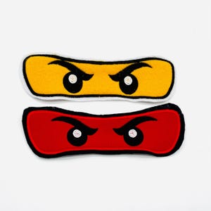 Könnte beinhalten: Zwei gestickte Aufnäher mit stilisierten Augen. Ein Aufnäher ist gelb mit schwarzen und weißen Augen, der andere ist rot mit schwarzen und weißen Augen. Beide Aufnäher haben eine schwarze Umrandung.