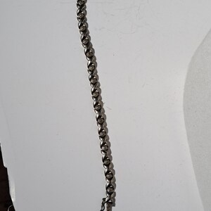 May include: A silver bracelet with a twisted design and small, round, clear stones.