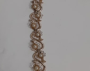 May include: A gold-tone bracelet with a delicate chain and a series of faux pearl flowers. The bracelet has a clasp closure.