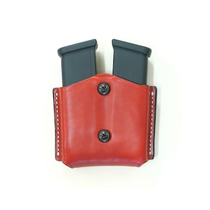 Peut inclure: Porte-chargeurs double en cuir rouge avec deux porte-chargeurs noirs. La pochette est dotée de deux fermetures à pression.