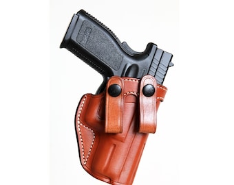Op de afbeelding: Een bruine leren holster met een zwart pistool erin. De holster heeft twee drukknopen aan de zijkant.