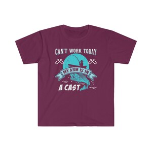May include: A maroon t-shirt with a blue graphic of a fisherman in a boat with the text "Can't work today, my arm is in a cast".