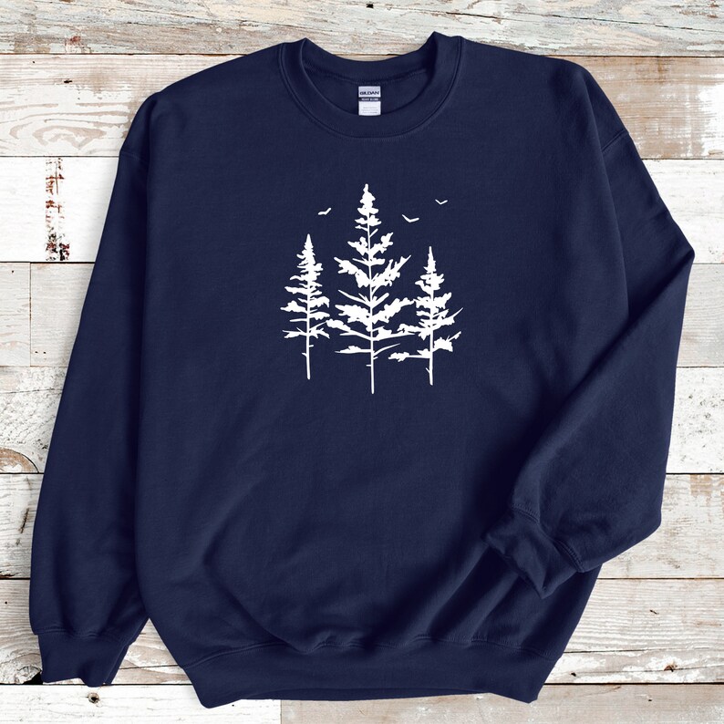 May include: A navy blue sweatshirt featuring a white silhouette of three pine trees with birds flying above them.