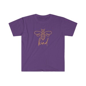 Puede incluir: Camiseta morada con un contorno dorado de una abeja y la palabra "kind" en cursiva. El dise&ntilde;o de la abeja est&aacute; centrado en la parte delantera de la camiseta. La camiseta tiene mangas cortas y cuello redondo.