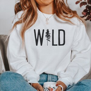 May include: White sweatshirt with the word "WILD" printed in black with a silhouette of a pine tree in the middle of the word.