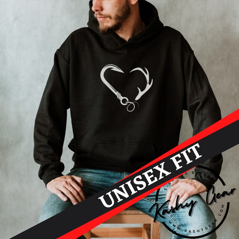 May include: Black unisex hoodie with a white heart-shaped design featuring a fishing hook and deer antlers. The hoodie has a front pocket and a hood. The words "UNISEX FIT" are printed on a diagonal black and red banner.
