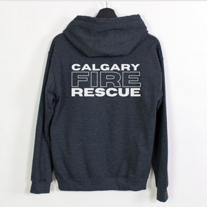 Peut inclure: Un sweat &agrave; capuche gris fonc&eacute; avec une fermeture &eacute;clair blanche. Le dos du sweat-shirt porte l'inscription "CALGARY FIRE RESCUE" en blanc.