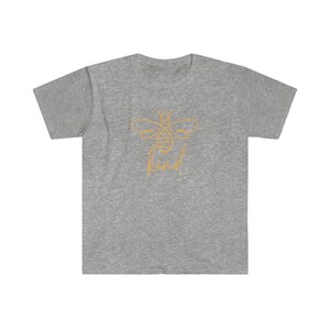 Puede incluir: Camiseta gris jaspeado con un contorno dorado de una abeja y la palabra "kind" debajo. El dise&ntilde;o est&aacute; centrado. La camiseta tiene mangas cortas y cuello redondo. La tela parece ser una mezcla suave de algod&oacute;n.